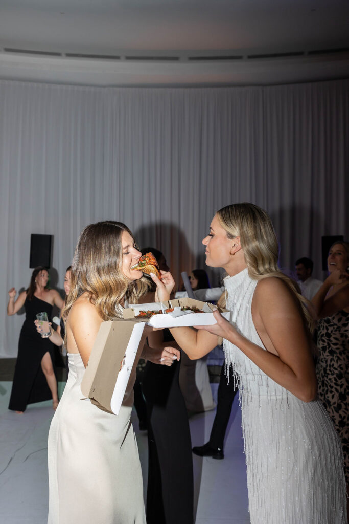 Bride feeding bridesmaids pizza at wedding reception 